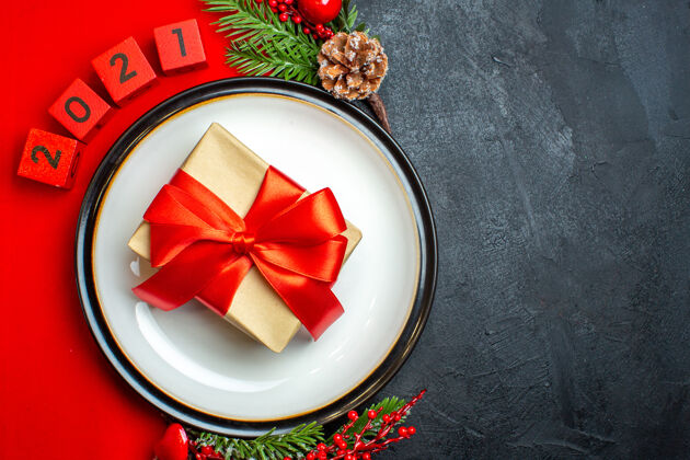 圣诞节新年背景与美丽的礼物在一个餐盘装饰配件杉木枝和数字在一个黑色的桌子上红色餐巾号码树枝冷杉