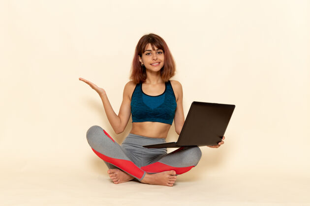 私人教练穿着蓝色衬衫 身体健康的年轻女性在白色墙上使用笔记本电脑的前视图坐着笔记本电脑锻炼