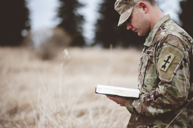 男性年轻的士兵在田野里读圣经诗歌保护者精神