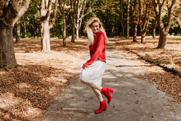 明亮微笑的金发女郎在秋天的公园里玩得很开心穿着时髦的红鞋子和白裙子跳舞颜色户外积极