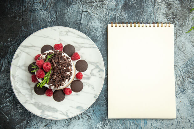 覆盆子顶视芝士蛋糕与巧克力和覆盆子白色椭圆形板记事本上的灰色表面托盘午餐美食