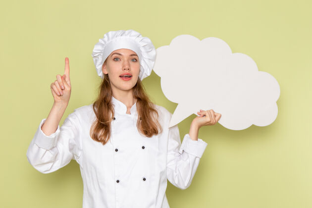 举行身穿白色厨师服的女厨师手持绿色墙上的白色标志的正面视图饭前面女