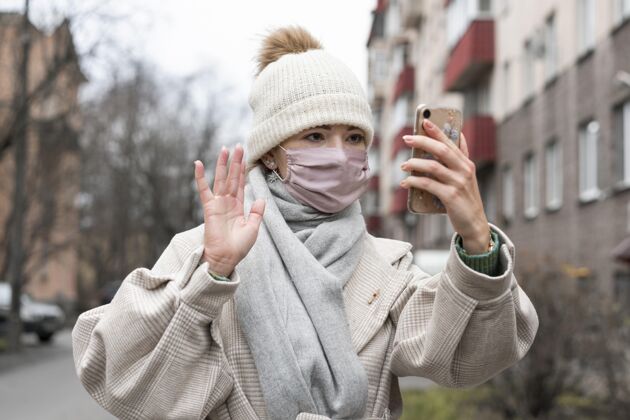 冠状病毒戴着医用面罩的女士正对着智能手机挥手大流行流行病女性