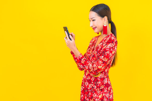 看肖像美丽的亚洲年轻女子在黄色墙壁上使用智能手机女孩女人聪明