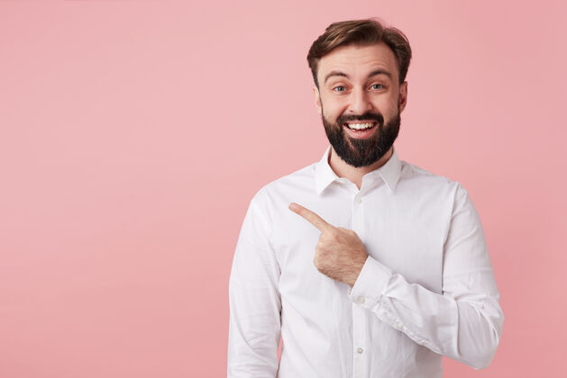 衣服喜气洋洋的留着棕色短发的年轻人的肖像 穿着正式的衣服 站在粉红色的墙上 食指指向一边 面带微笑爱情男性短裤