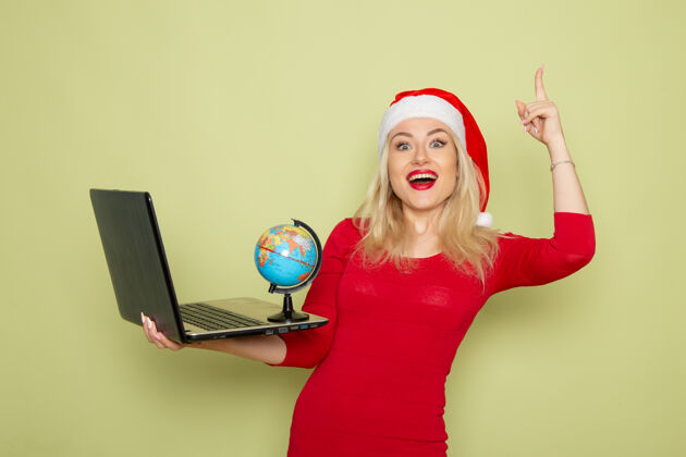 雪正面图美丽的女性手持小地球仪 在绿墙上使用笔记本电脑圣诞色雪地新年感慨圣诞节颜色情感