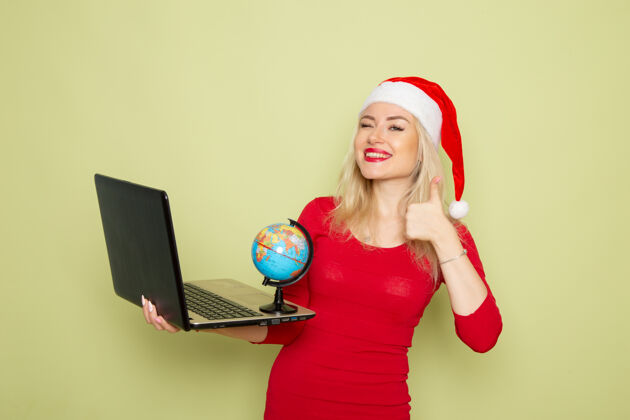 金发正面图美女手持小地球仪 在绿墙上用笔记本电脑彩雪过年感慨笔记本电脑漂亮的女人圣诞节