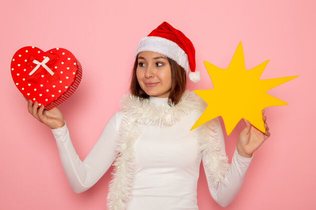颜色正面图年轻女性手持黄色的身影 呈现在粉色墙壁上雪地圣诞色节日新年时尚雪风景帽子
