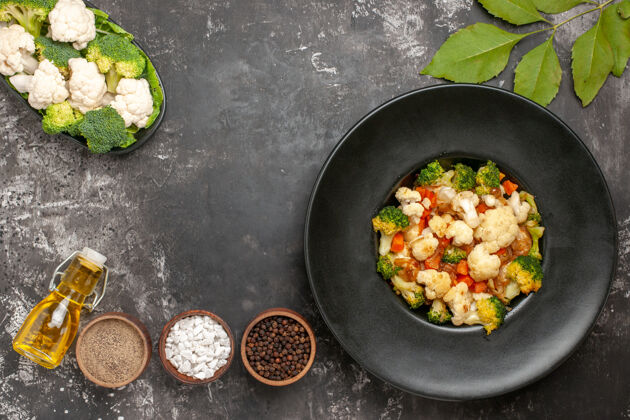 观点顶视图西兰花和花椰菜沙拉在黑色碗不同的香料在碗油生蔬菜在黑暗的表面盘子锅碗沙拉