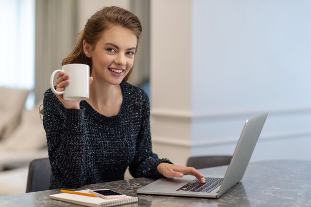 微笑美丽的年轻微笑的女人坐在家里一边工作一边喝咖啡女性白种人使用