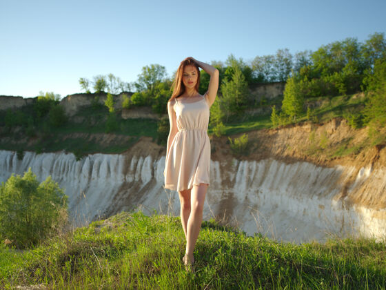 白种人模特在一个阳光明媚的日子摆姿势 周围是一片阳光灿烂的风景年轻女子站在悬崖边 背后是美丽的景色穿着白色连衣裙的漂亮女孩在户外摆姿势休闲看坐着