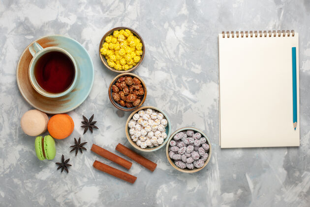 茶在浅白色的桌子上 可以俯瞰一杯茶 里面有糖果和法式马卡龙顶部糖果美味