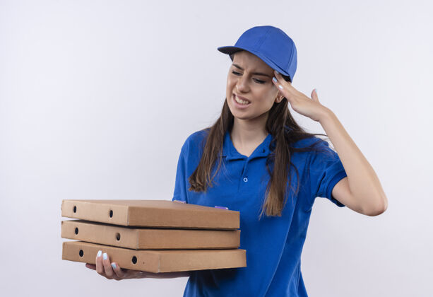 送货穿着蓝色制服 戴着帽子 拿着披萨盒的年轻送货女孩看起来很疲惫 工作过度 摸着头感觉很痛触摸看疼痛