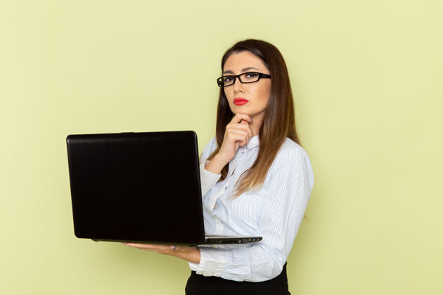 办公室穿着白衬衫和黑裙子的女上班族在浅绿色墙上使用笔记本电脑的正视图商务衬衫电脑