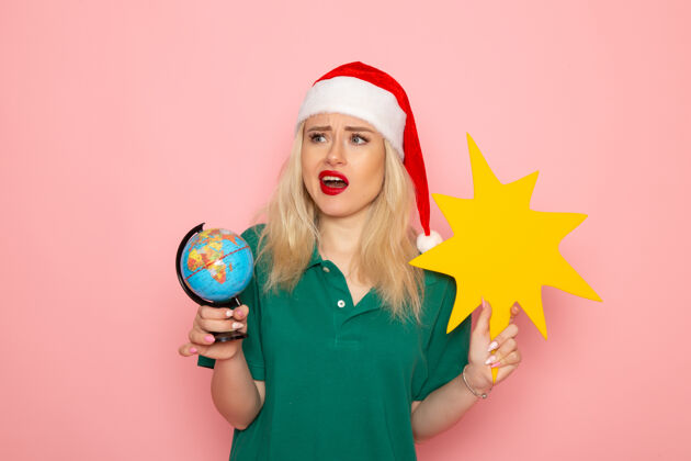 年轻的女人正面图年轻女性手持地球仪和粉红色墙上的黄色人物照片模特女子圣诞节新年彩色假期风景地球仪肖像