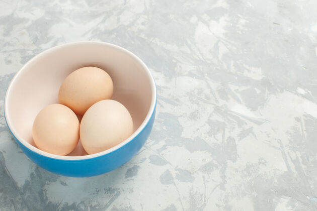 早餐正面图浅白色桌子上的小盘子里的生鸡蛋晚餐鸡肉前面