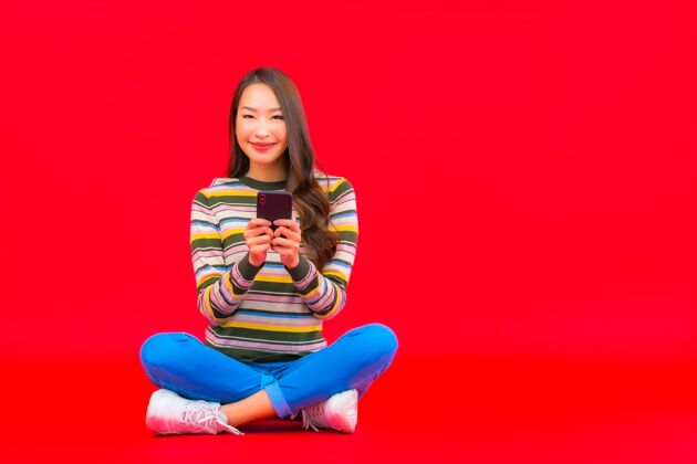 科技肖像美丽的亚洲年轻女子在红色隔离墙上使用智能手机文字手机手机
