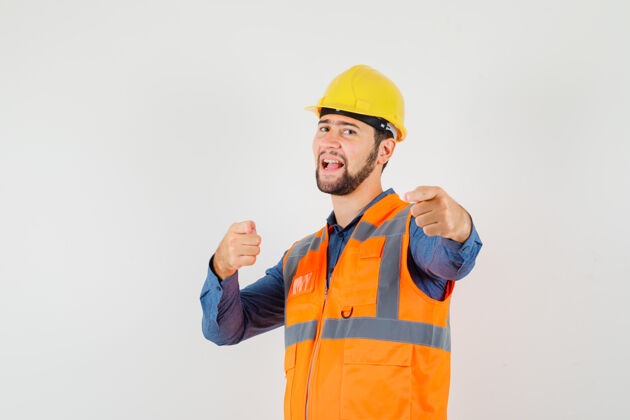 工具年轻的建筑工人指着摄像机 穿着衬衫 背心 戴着头盔 看上去很自信正面建筑职业