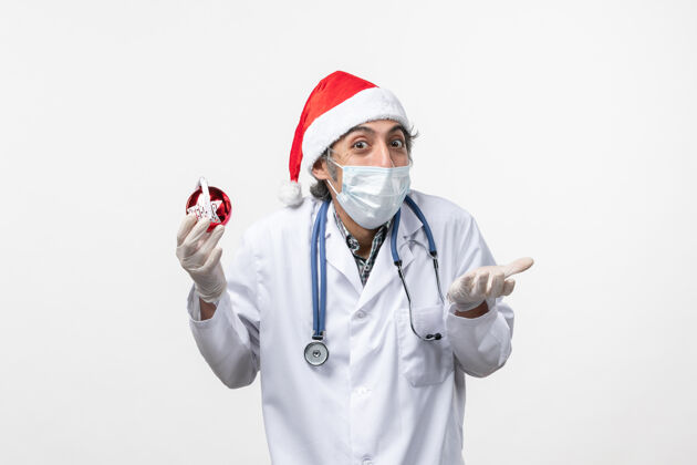 圣诞节正面图白墙上戴着玩具面具的男医生健康假日病毒外套实验室外套药品