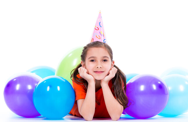 情感穿着橙色t恤的快乐微笑女孩躺在地板上 带着五颜六色的气球-孤立在白色的地板上乐趣女性美丽