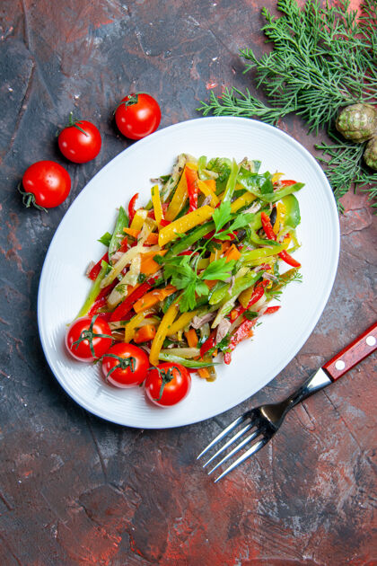 蔬菜沙拉俯视图蔬菜沙拉在椭圆形盘子叉樱桃西红柿在深红色的桌子上蔬菜膳食番茄