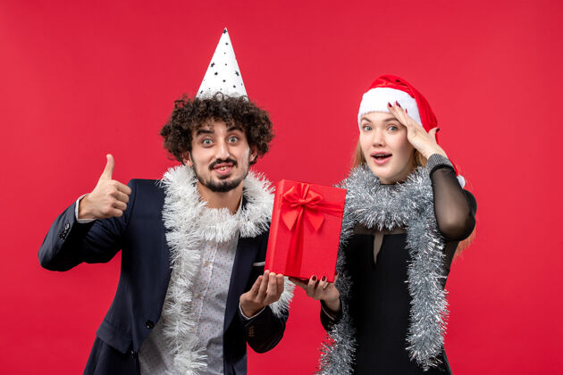 服装正面图一对年轻夫妇手持新年礼物站在红墙上感慨爱圣诞圣诞节情感成人