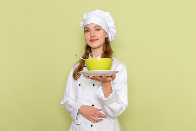 套装身着白色厨师服的女厨师微笑着拿着绿色的盘子站在绿色的墙上盘子人烹饪