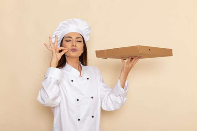 烹饪身穿白色厨师服的年轻女厨师正拿着食物盒站在浅白的墙上成人医生人