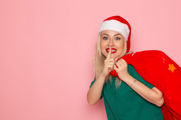 圣诞老人正面图：年轻女性提着红包 在粉色墙上贴着礼物圣诞老人的新年照片年轻女性圣诞节肖像
