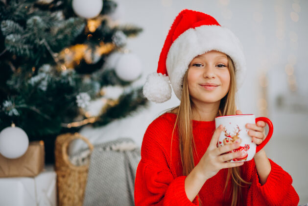 乐趣在圣诞树旁喝可可的女孩少年女孩爱
