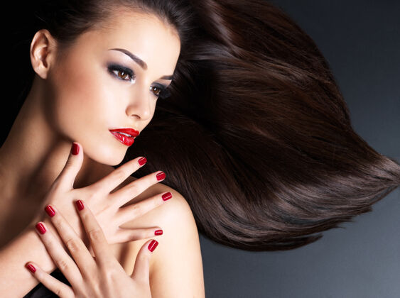 女孩长着棕色直发和红指甲的漂亮女人躺在黑暗的墙上头发美甲黑发