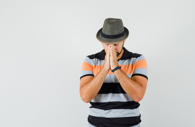 肖像年轻人手牵手在祈祷的姿态在t恤衫 帽子和期待 正面视图休闲成人男人
