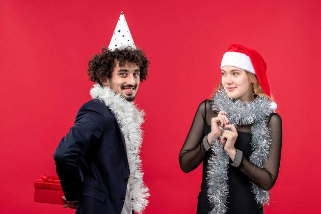快乐正面图：年轻夫妇在红墙上拿着新年礼物 他们热爱圣诞节风景微笑肖像