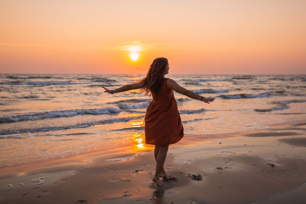 性感一个穿着棕色太阳裙的模特在海滩享受日落的美丽照片风格水头发