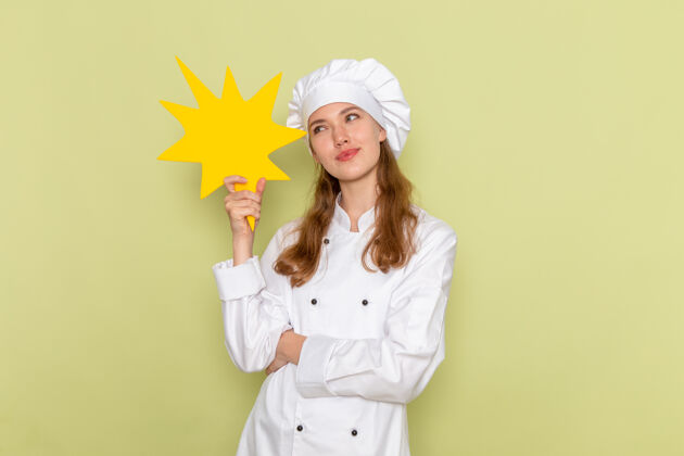 举行身着白色厨具套装的女厨师正对着绿色墙上的黄色标牌思考套装人肖像