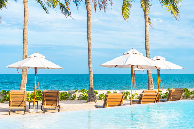 蓝色酒店度假区的户外游泳池周围有雨伞和躺椅 有海边沙滩和椰子树棕榈甲板椅天空