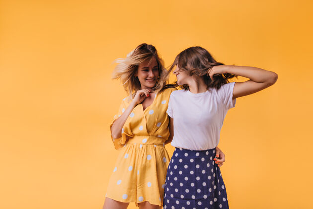 年轻一个穿着黄色衣服的年轻女子微笑着看着朋友快乐的高加索姐妹们在橙色上发冷情感女性寒冷
