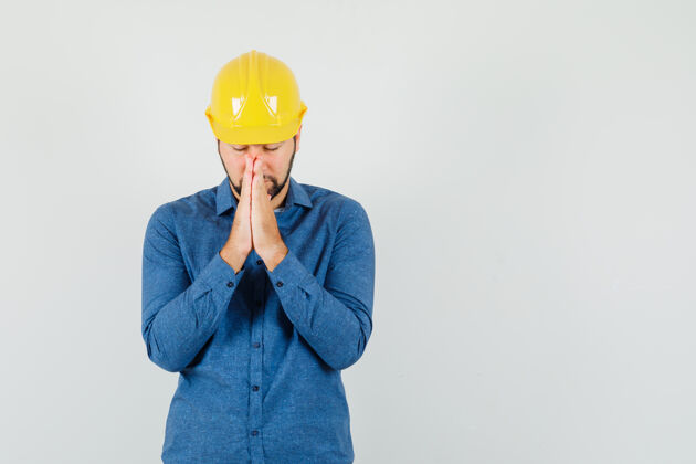 手年轻的工人穿着衬衫 戴着头盔 手举祈祷的姿势 看上去很平静举行分析会议