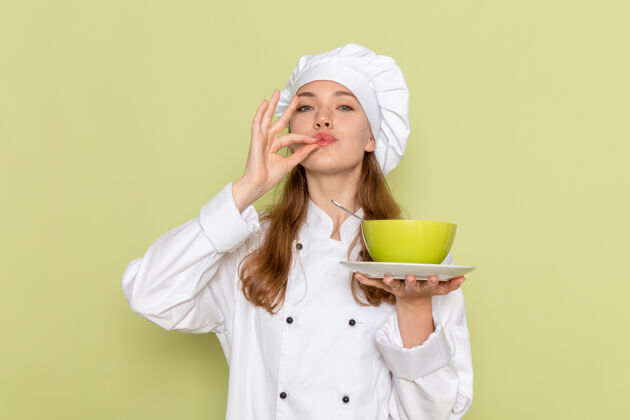 人身穿白色厨师服的女厨师正拿着绿盘子 绿墙上放着汤厨房肖像烹饪