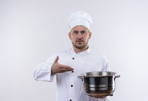 厨师年轻帅气的厨师穿着厨师制服 手拿着锅 指着锅 看着孤立的白色空间年轻指着锅