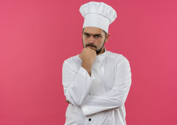 厨师穿着厨师制服的年轻男厨师把拳头放在下巴上隔离在粉红色的空间里空间放男性