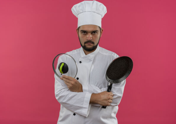 看穿着厨师制服的年轻男厨师手拿煎锅和锅盖 看上去在粉红色的空间里与世隔绝男性薯条盖子