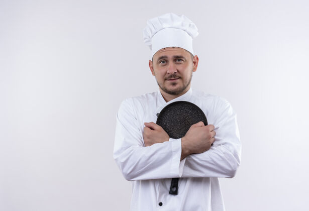 厨师高兴的年轻帅哥厨师穿着厨师制服拿着煎锅隔离在白色的空间平底锅手持油炸