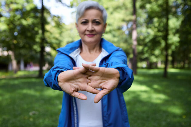 老年人迷人的白发成熟的白人妇女穿着蓝色外套伸出手来 伸展手臂和双手 在早晨户外训练时做热身动作选择性地集中在手掌上老年人成年人能量