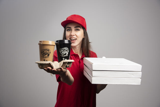饮料送披萨和咖啡杯的女人站在灰色的墙上女性食物快递
