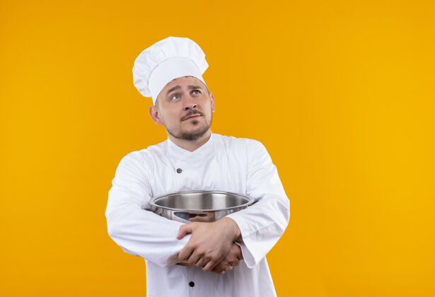 厨师体贴的年轻帅哥厨师穿着厨师制服拿着锅炉仰望孤立的橙色空间体贴厨师帅气