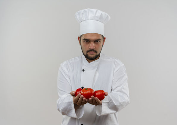 不愉快穿着厨师制服 拿着西红柿的年轻男厨师看起来被隔离在空白处看制服年轻