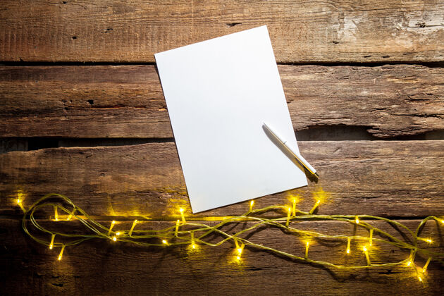 庆祝在木桌上放一张白纸 上面有钢笔和圣诞装饰品信制造花环