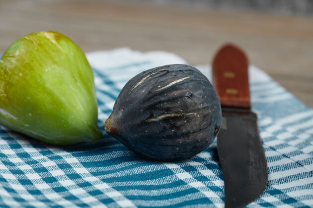 新鲜两个无花果和一把刀 木桌上放一块蓝色桌布水果木制黑色