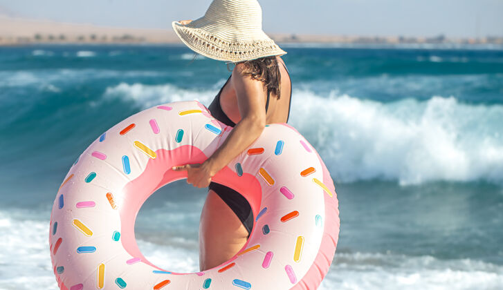 年轻一个戴着帽子的女人 戴着一个甜甜圈 在海边游泳度假休闲娱乐的概念夏天阳光女人